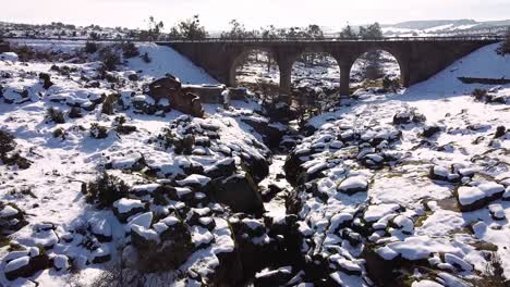 Serial-view-of-a-drone-flying-over-a-nice-snowy-field-with-a-river-and-an-old-car-crossing-a-bridge