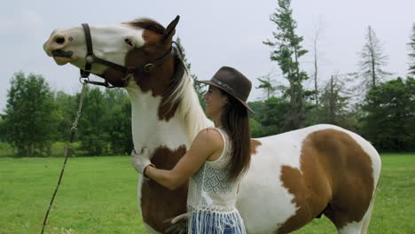 Confident-young-cowgirl-bonding-with-her-adult-male-pinto-horse,-rubbing-his-neck