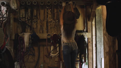 Cowgirl-grabs-her-horse-riding-gear-off-the-wall-of-a-rustic-old-barn-1