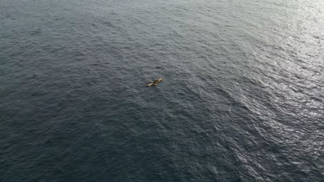 Aerial-orbit-shot-of-a-single-Kayak-over-the-ocean-with-sun-reflecting-the-ocean-water