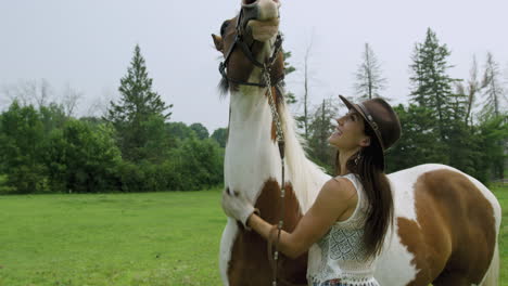 Trained-young-cowgirl-rubs-her-pinto-horse's-neck,-laughing-at-the-horse's-obvious-enjoyment