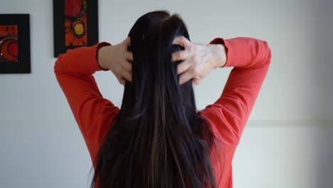 Rear-View-Of-Adult-Woman-Brushing-Her-Long-Black-Hair-Up-With-Fingers