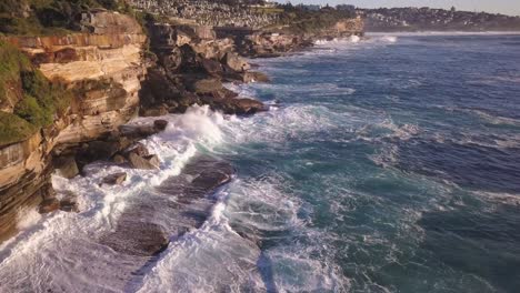 Low-aerial-shot-of-Sydney-coast,-waves-hitting-the-rocks-at-Clovelly-Cemetery