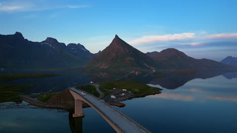 Car-driving-over-famous-bridges-on-Lofoten-Island,-Fredvang,-with-reflecting-mountains-on-the-surface