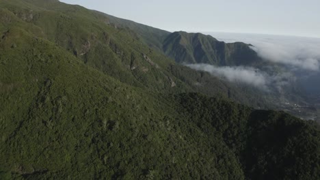 Toma-Aérea-Sobre-La-Isla-De-Madeira-Con-Nubes-Bailando-Alrededor-De-La-Montaña-Y-El-Valle-En-La-Distancia
