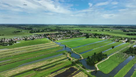 High-wide-aerial-shot-of-a-typical-dutch-polder-land-with-many-small-canals-and-slagenlandschap-surrounding-a-town-with-blue-skies-and-clouds-in-the-Krimpenerwaard-region-of-Netherlands