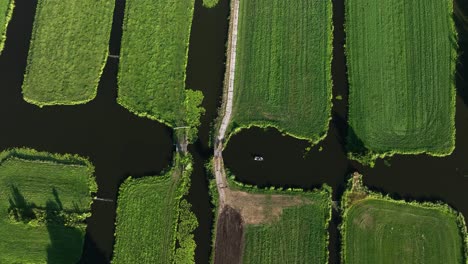 Dramatic-aerial-view-of-canals-and-waterways-in-a-polder-land-with-dark-waters-and-vivid-green-fields,-and-a-small-boat-cruising-in-the-water,-Netherlands