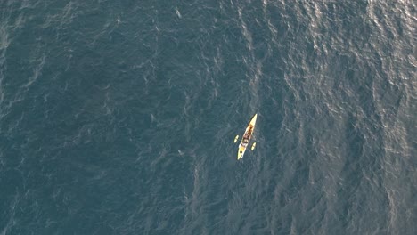 Aerial-top-down-view-of-a-yellow-single-fishing-kayak-floating-on-the-ocean-with-morning-sun-reflection