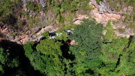 Descending-drone-aerial-shot-of-the-cave-entrance-to-the-Enchanted-Well-or-Poço-Encantado-surrounded-by-tropical-trees,-plants,-and-cliffs-in-the-Chapada-Diamantina-National-Park-in-Northern-Brazil
