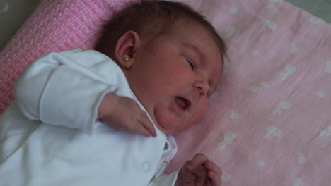 Newborn-baby-girl-yawns,-stretches-and-wiggles-while-lying-on-pink-blanket