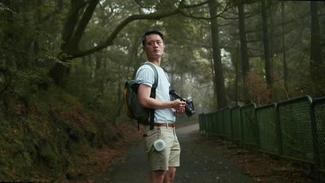 Un-Joven-Fotógrafo-Asiático-Con-Una-Camiseta-Blanca-Y-Una-Mochila-Está-Tomando-Fotografías-De-La-Naturaleza-En-El-Bosque,-Ubicado-En-Taiwán