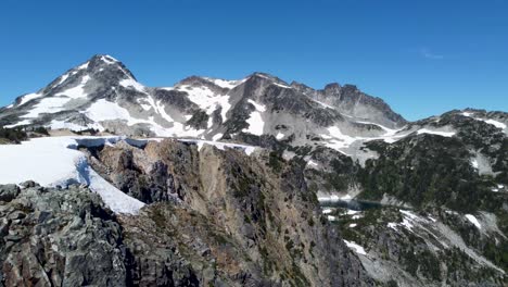 Bergspitzen-Landschaftsschwenk-Mit-Luftdrohne-Mit-Schnee-Und-Kiefern-Und-Strahlend-Blauem-Himmel