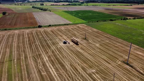 Arial-drone-shot-of-farmer-collecting-hay-rolls-from-the-field