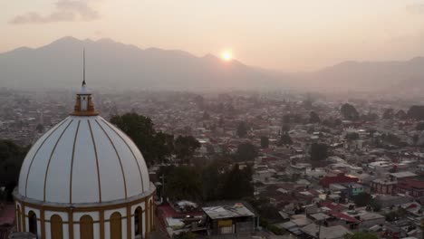 Drone-passing-by-Guadalupe-Church-during-sunset-tilting-up-and-showing-the-City-of-San-Cristobal-de-las-Casas,-Chiapas,-Mexico