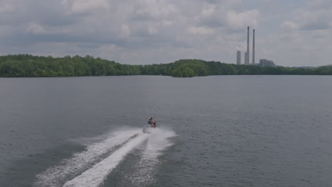 Slow-motion-aerial-footage-of-a-jet-ski-on-a-lake-with-a-power-plant-in-the-background