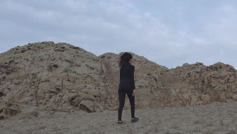 Long-slow-motion-shot-of-a-mysterious-woman-dressed-in-black-walking-in-the-desert-between-mountains-of-sand