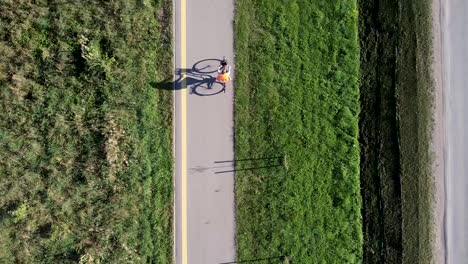 Arial-drone-shot-of-cyclist-women-with-a-high-visible-jacket-on-a-bicycle-road