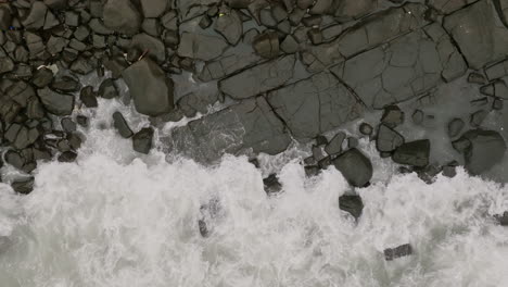 Slow-motion-aerial-footage-pedestaling-up-of-ocean-waves-crashing-into-rocks