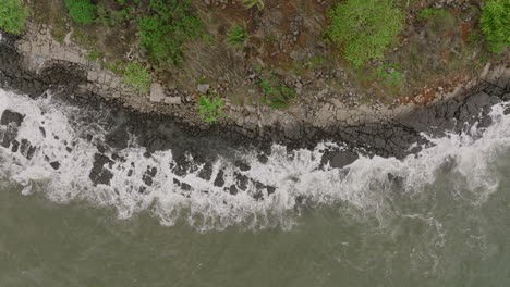 Slow-motion-aerial-footage-top-down-of-ocean-waves-crashing-into-rocks
