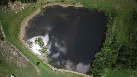 Top-down-aerial-hyperlapse-of-a-pond-with-puffy-white-clouds-reflecting-on-the-surface