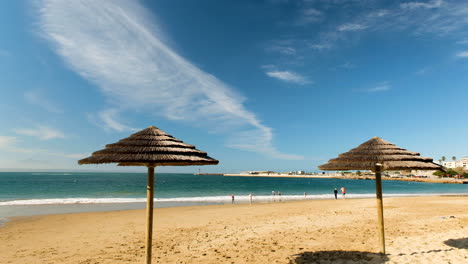 Dos-Sombrillas-De-Paja-En-La-Playa-De-Santos,-Clima-Encantador-Con-Gente-Nadando
