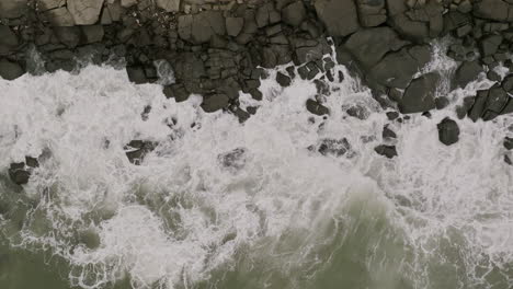 Breite-Luftaufnahmen-In-Zeitlupe-Von-Oben-Nach-Unten-Von-Meereswellen,-Die-Gegen-Felsen-Prallen