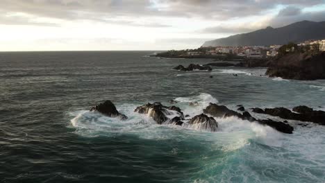 Wave-crashing-on-rocks-in-Tenerife,-with-Los-Gigantes-cliffs-in-the-background