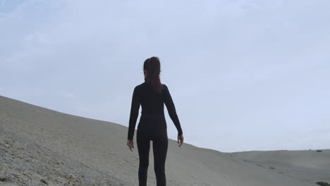 Mysterious-woman-dressed-in-black-from-the-back-looking-at-the-desert-while-the-wind-blows-strong-in-slow-motion