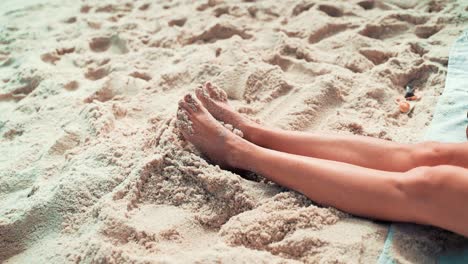 Woman-stretching-her-legs-in-the-sand-and-wiggling-her-toes-as-a-sign-of-relaxation,-relaxing-sunny-day-with-copy-space
