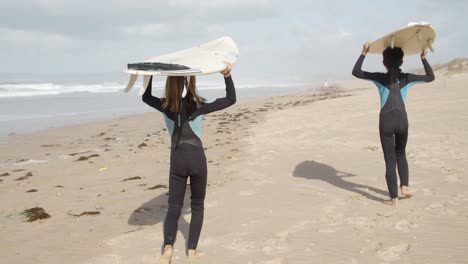 Unrecognizable-young-children-with-a-surfboard-and-wetsuit-walking-in-the-beach-during-a-recreating-activity-in-vacations