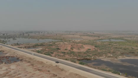 Drone-Captura-La-Vista-Aérea-Del-Automóvil-Que-Conduce-A-Través-De-La-Carretera-Con-árboles-Al-Costado-De-La-Carretera-Cerca-De-Khairpur,-Sindh,-Pakistán