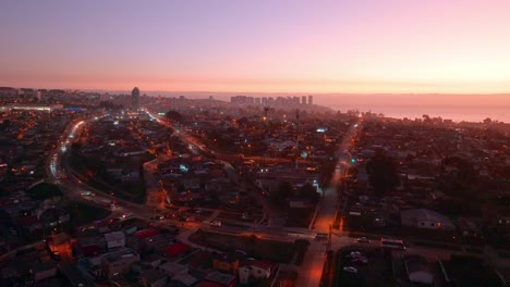 Dolly-in-aerial-view-of-a-sunset-in-a-lower-class-neighborhood-with-traffic-in-Concon,-Chile