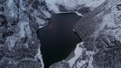 Lake-Braies-in-winter-during-sunrise-hidden-between-Dolomites-mountain-peaks,-aerial