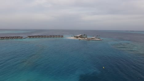 Drone-shot-of-a-Maldives-Island-in-the-middle-of-the-ocean,-with-water-villas