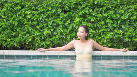 A-woman-stretches-her-arms-out-along-the-side-of-a-pool