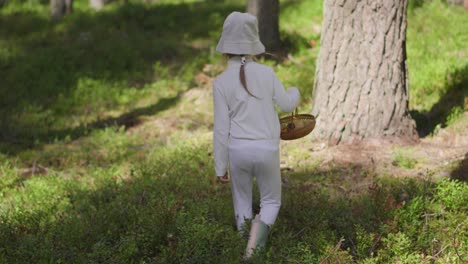 A-young-female-child-walking-in-the-forest-with-a-basket-picking-blueberries-and-mushrooms-during-the-summer