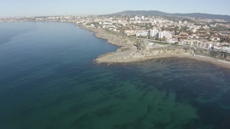 Aerial-drone-view-of-Estoril-Beach-in-São-Pedro-do-Estoril,-Greater-Lisbon,-Cascais-in-background