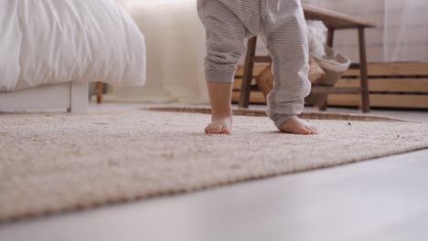 Baby-first-steps-inside-the-bedroom,-unrecognizable-toddler-balancing-and-learning-how-to-walk