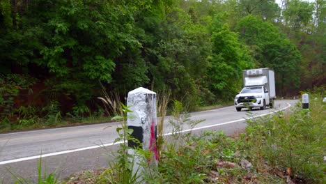 Shot-of-a-white-van-passing-by-over-a-winding-road-along-the-hilly-terrain-in-North-Thailand-at-daytime