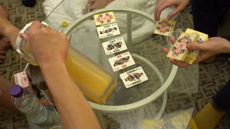 Eine-Gruppe-Von-Freunden,-Die-In-Hong-Kong-Karten-Spielen,-Während-Sie-Saft-Auf-Einem-Glastisch-Trinken