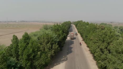 The-Pakistani-highway-in-Khairpur-Sindh-is-lined-with-thick-green-trees,-providing-a-lovely-view-of-the-moving-ar