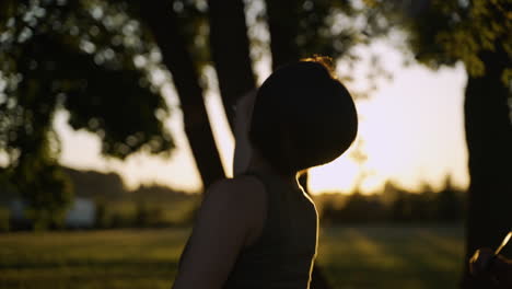 Woman-with-short-hair-in-a-tank-top-plays-badminton-in-a-field-as-the-sun-sets-in-the-background