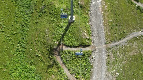 Top-drone-view-of-gondolas-and-metal-poles-crossing-a-grass-field-in-the-Swiss-alps,-Obwalden-and-a-downhill-bike-path
