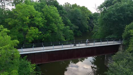 Person-rides-bicycle-across-bridge-over-stream