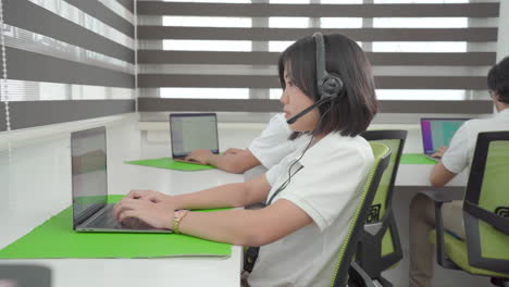 Asiatische-Frau-Mit-Headsets,-Die-Arbeitet,-Um-Kunden-Auf-Computer-laptops-In-Einem-Modernen-Büro-Zu-Unterstützen