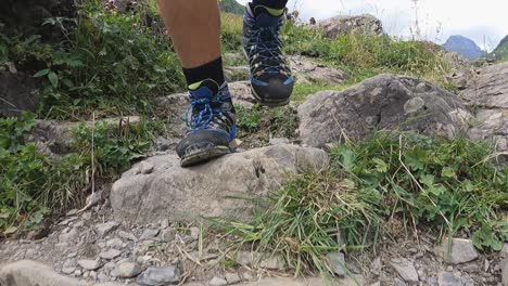 Front-view-of-a-man-walking-in-the-swiss-alps-with-trail-shoes,-walking-on-rocks,-grass