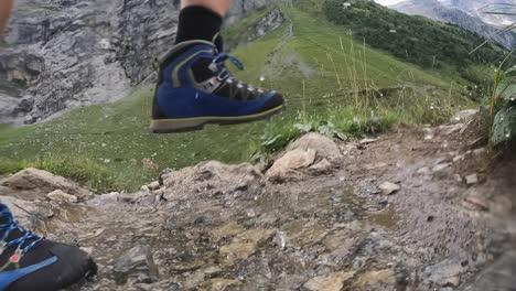 A-man-walks-on-a-natural-path-in-the-swiss-alps-and-splashes-water-with-his-shoes-form-a-small-river-going-down-the-mountain,-Obwald,-Engelberg,-side-view