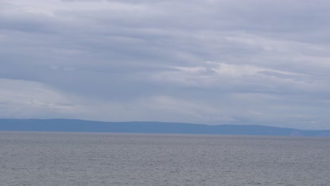 An-outstanding-view-of-the-seashore-with-mountains-behind-under-a-gray-cloudy-day