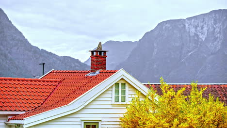 A-house-in-the-foreground-with-rugged-mountains-and-cliffs-in-the-background-at-daytime-with-an-overcast-sky---time-lapse