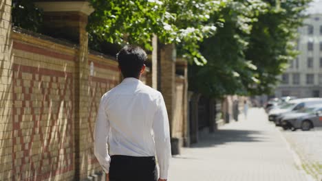 Rear-view-of-man-wearing-white-shirt-walking-on-Riga-streets,-sunny-day